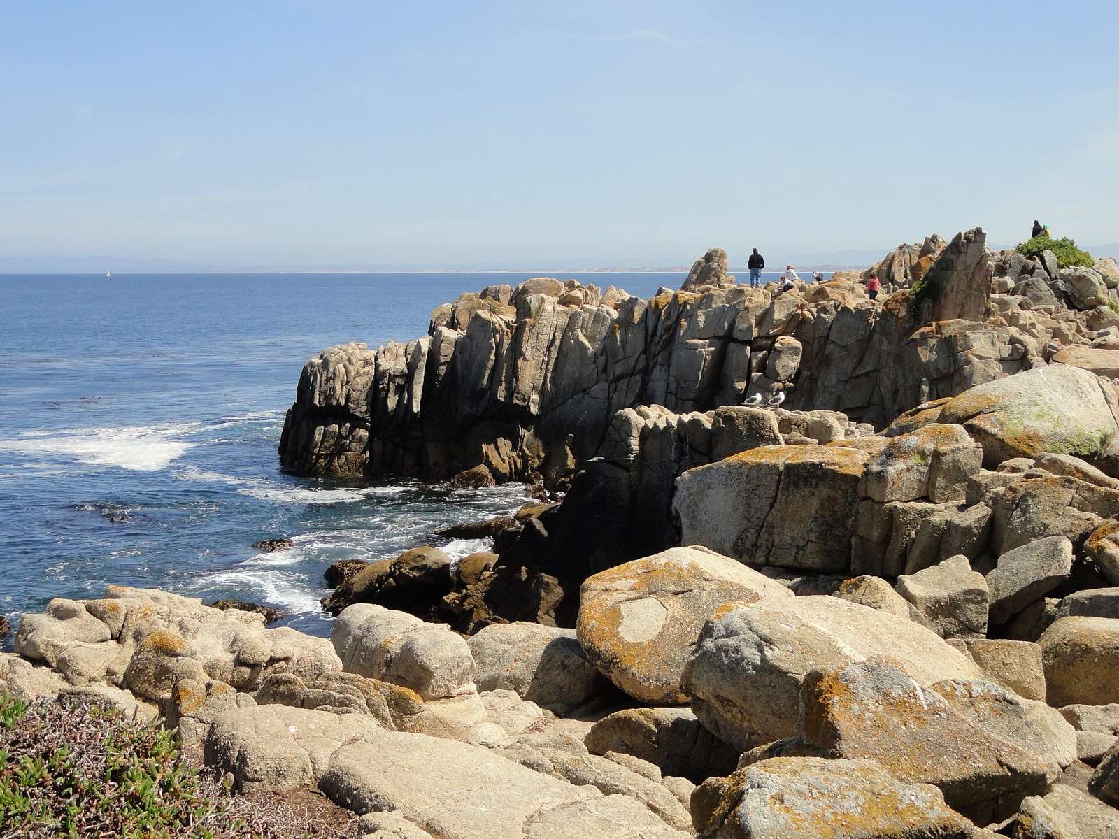 Granite outcrops, Pacific surf, and visitors along the rocky shoreline at Lovers Point Park.