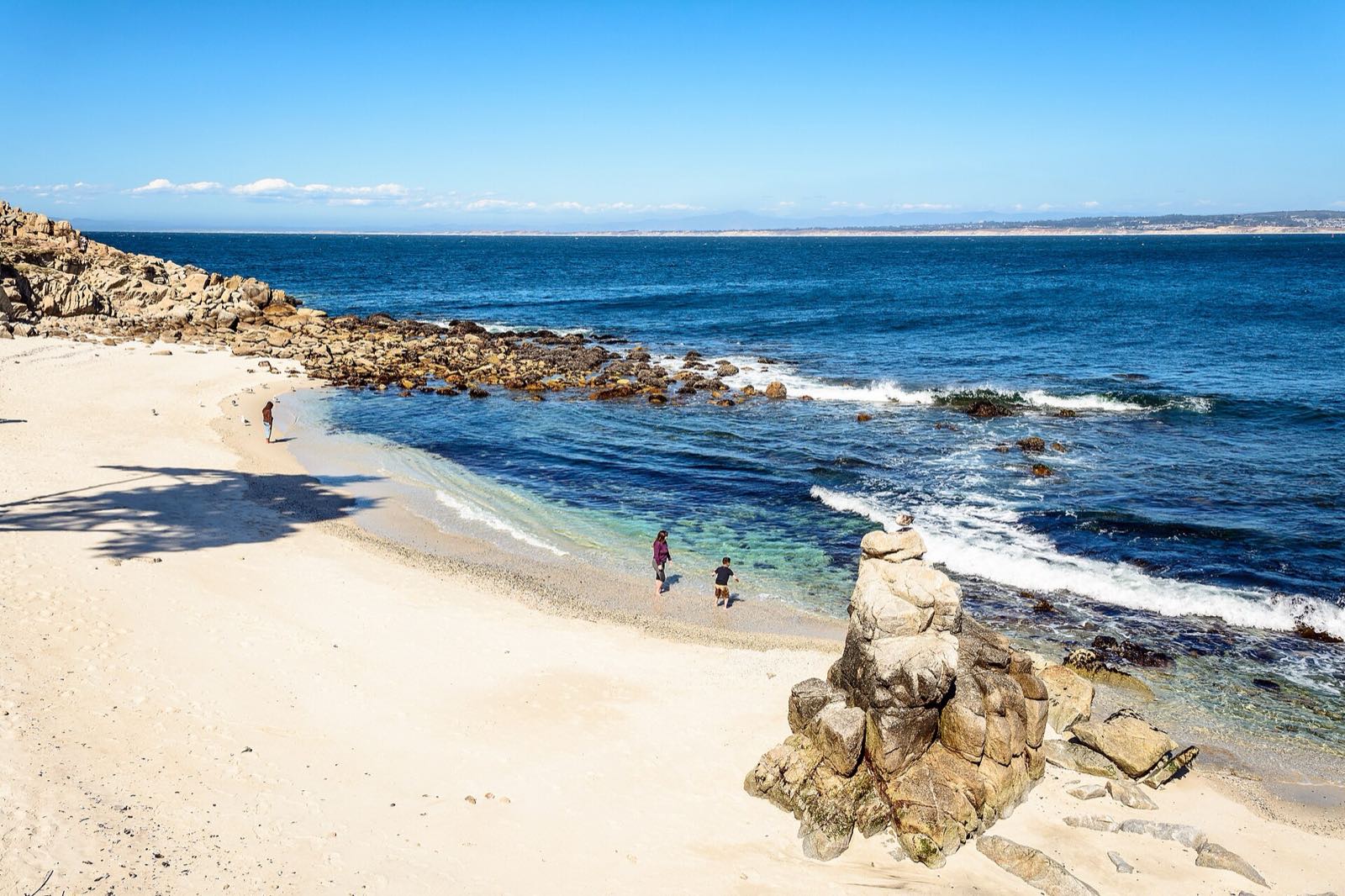 Small sandy cove, rocky shoreline, and blue Pacific water in Pacific Grove.